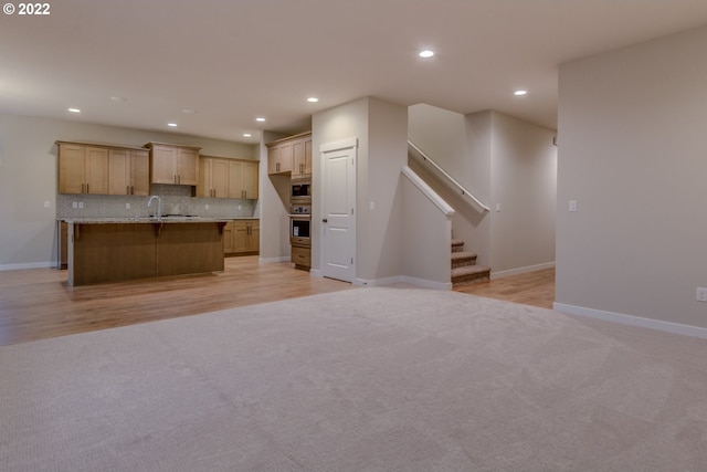 kitchen with built in microwave, sink, backsplash, an island with sink, and light colored carpet