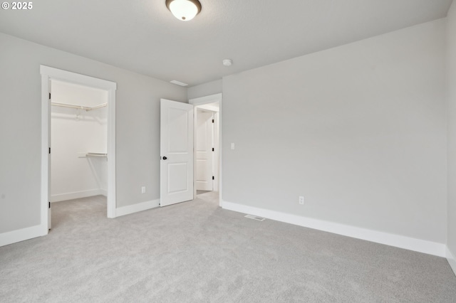 unfurnished bedroom with a walk in closet, light colored carpet, and a closet