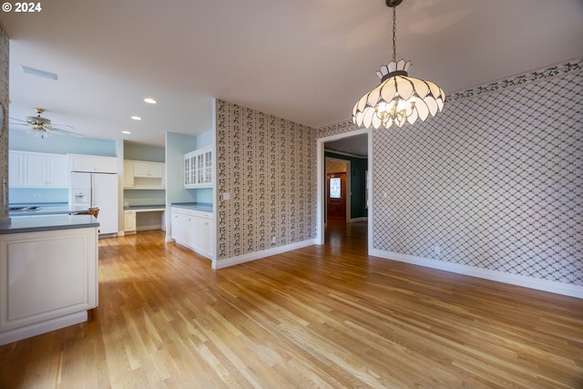 unfurnished dining area with ceiling fan with notable chandelier and light hardwood / wood-style floors