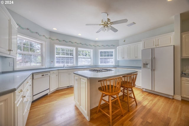 kitchen with white cabinets, light hardwood / wood-style flooring, a kitchen island, and white appliances