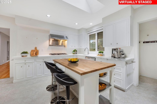 kitchen with exhaust hood, a kitchen breakfast bar, stainless steel appliances, white cabinets, and butcher block counters