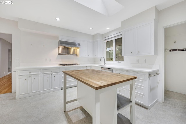 kitchen with appliances with stainless steel finishes, exhaust hood, white cabinetry, butcher block counters, and a breakfast bar area