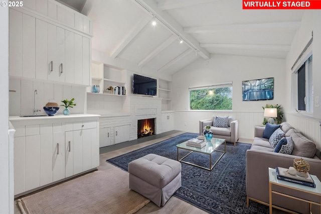 living room with rail lighting, built in features, lofted ceiling with beams, and a fireplace