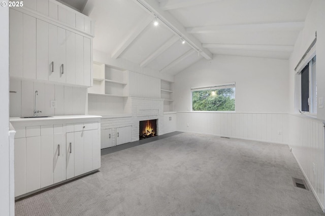 unfurnished living room featuring a brick fireplace, built in shelves, light colored carpet, vaulted ceiling with beams, and sink