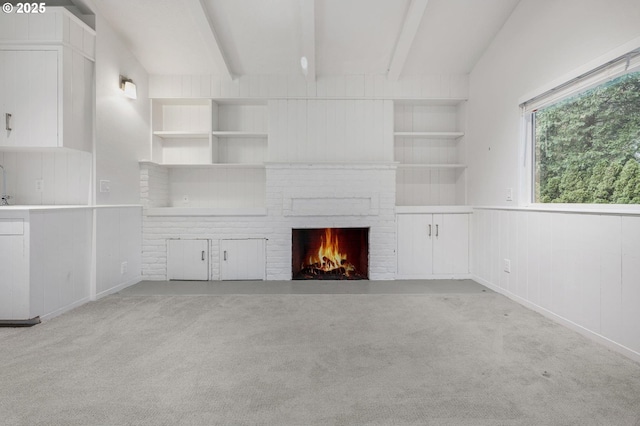 unfurnished living room featuring light carpet, built in shelves, a fireplace, and vaulted ceiling with beams