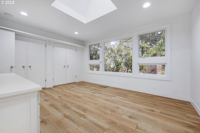 unfurnished dining area featuring a skylight and light wood-type flooring