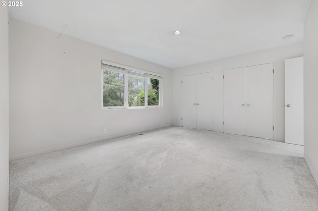 unfurnished bedroom featuring light colored carpet and multiple closets