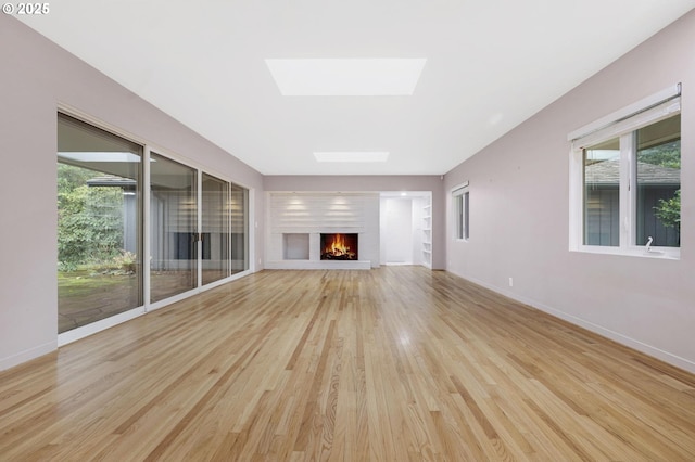 unfurnished living room with light wood-type flooring and a skylight