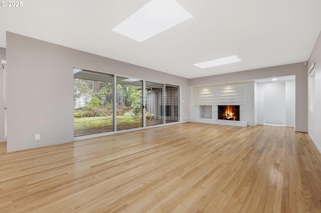 unfurnished living room with a brick fireplace, a skylight, and light hardwood / wood-style flooring