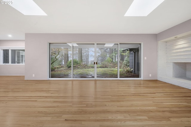 unfurnished living room featuring light hardwood / wood-style flooring, a skylight, and a fireplace