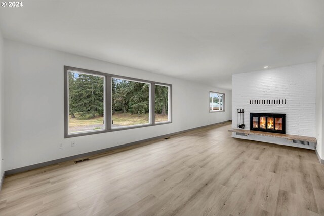 unfurnished living room with brick wall, a healthy amount of sunlight, a brick fireplace, and light hardwood / wood-style floors