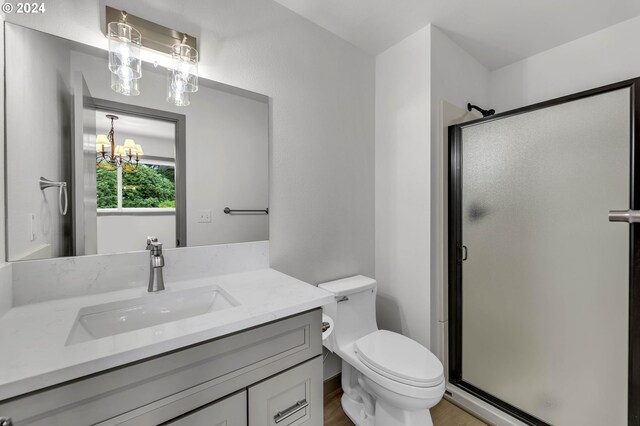 bathroom with a shower with door, vanity, an inviting chandelier, toilet, and hardwood / wood-style flooring