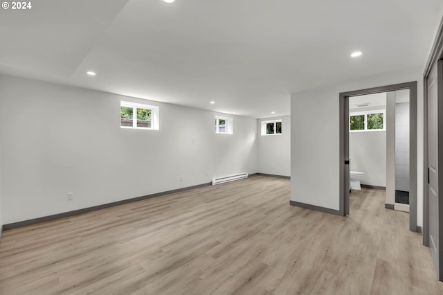 basement with a baseboard heating unit, a wealth of natural light, and light hardwood / wood-style floors