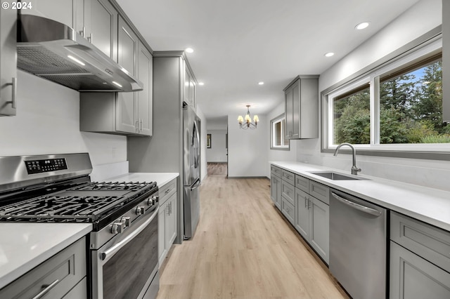 kitchen with gray cabinetry, a notable chandelier, appliances with stainless steel finishes, sink, and light wood-type flooring