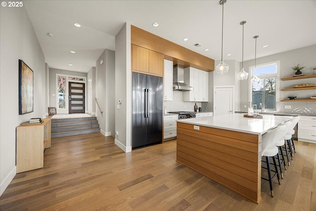 kitchen with tasteful backsplash, built in refrigerator, a kitchen island, white cabinets, and wall chimney range hood