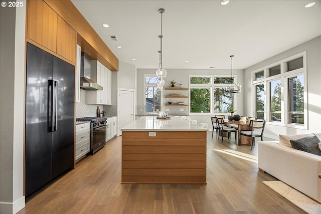 kitchen with pendant lighting, high quality appliances, white cabinets, decorative backsplash, and wall chimney exhaust hood