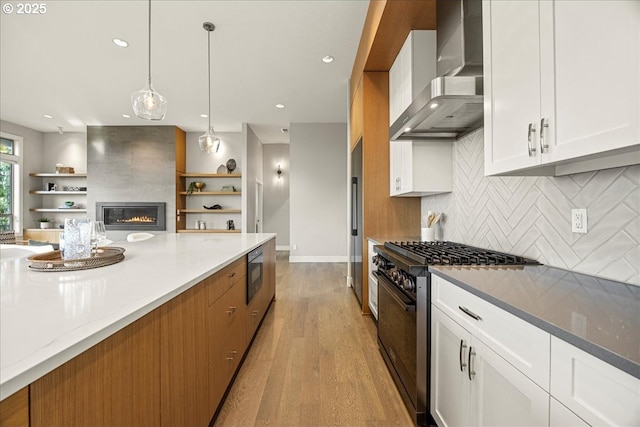 kitchen with open shelves, premium appliances, light wood-style flooring, and wall chimney exhaust hood
