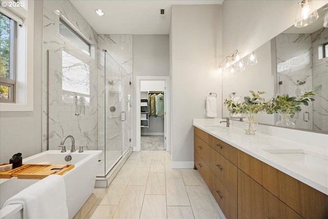 full bath with double vanity, a walk in closet, a stall shower, a sink, and a soaking tub