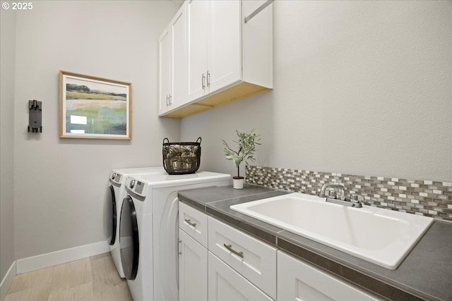 clothes washing area featuring cabinet space, baseboards, a sink, and washer and dryer
