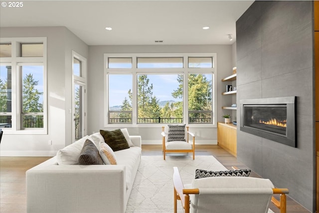 living room featuring built in shelves, light hardwood / wood-style floors, and a tile fireplace