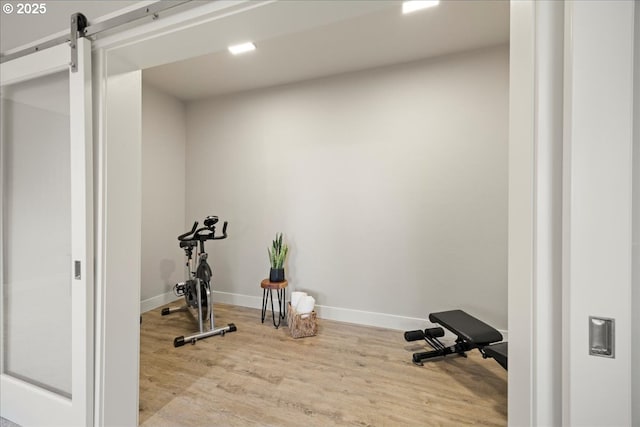 workout room with a barn door and light wood-type flooring