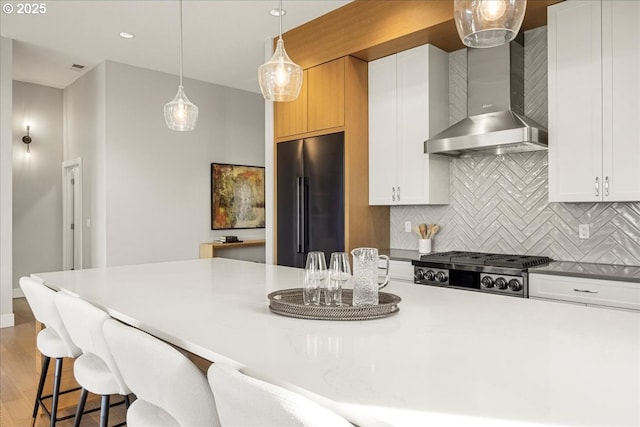 kitchen with high end fridge, wall chimney range hood, and white cabinetry