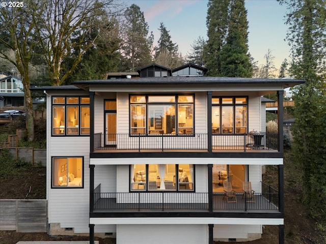 back of house at dusk with crawl space and a balcony