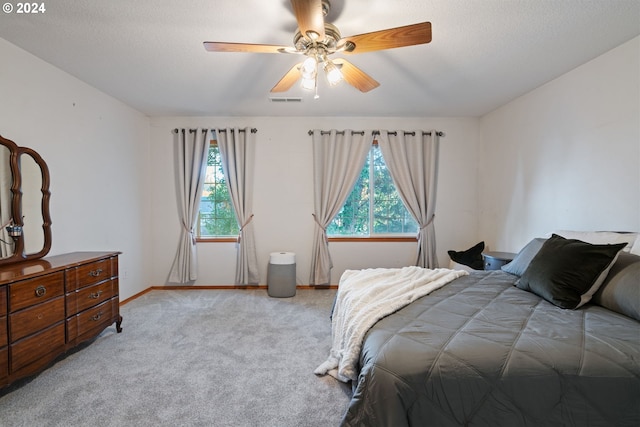 bedroom featuring ceiling fan, light colored carpet, a textured ceiling, and multiple windows