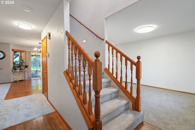 stairs featuring carpet, a textured ceiling, and an inviting chandelier