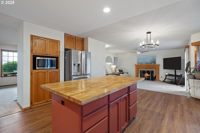 kitchen with wooden counters, hardwood / wood-style flooring, decorative light fixtures, a kitchen island, and stainless steel appliances