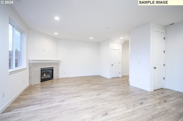 unfurnished living room with light wood-type flooring and a tile fireplace