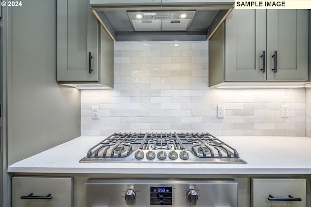 kitchen featuring stainless steel appliances, light stone counters, ventilation hood, gray cabinets, and decorative backsplash