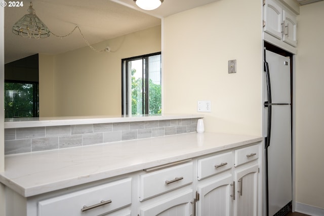 kitchen with tasteful backsplash, light stone counters, white cabinetry, and white refrigerator