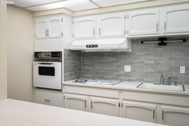 kitchen with premium range hood, white cabinets, sink, oven, and gas stovetop