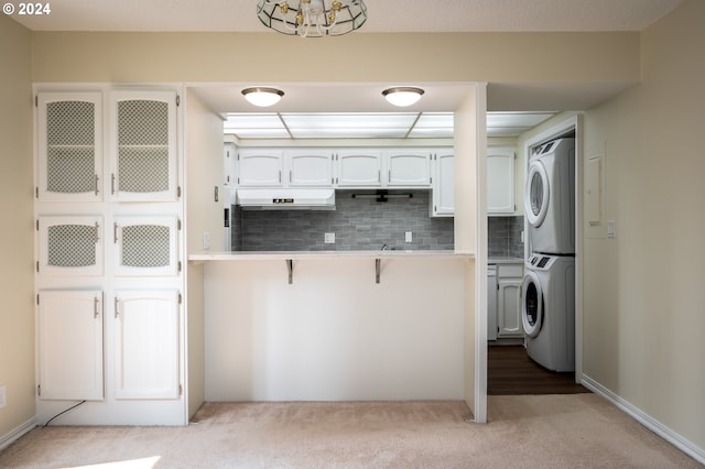 kitchen with tasteful backsplash, stacked washer / drying machine, white cabinets, and light carpet