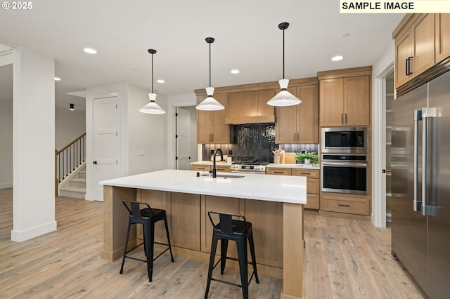 kitchen with pendant lighting, a center island with sink, light countertops, appliances with stainless steel finishes, and a sink