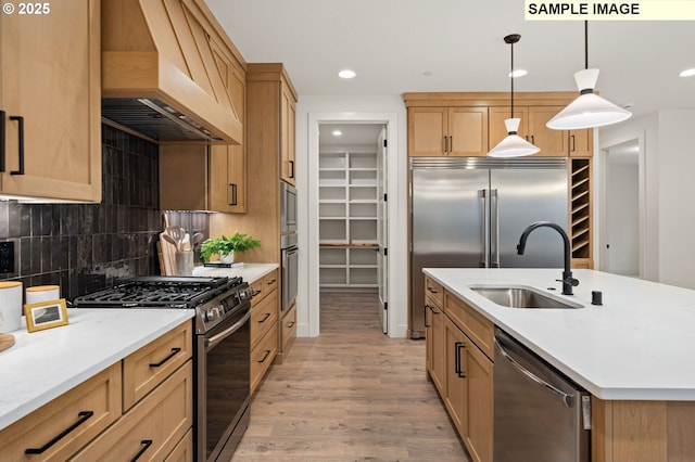 kitchen featuring pendant lighting, custom range hood, appliances with stainless steel finishes, a sink, and an island with sink