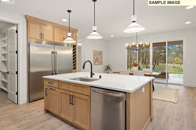 kitchen with a center island with sink, hanging light fixtures, stainless steel appliances, light countertops, and a sink