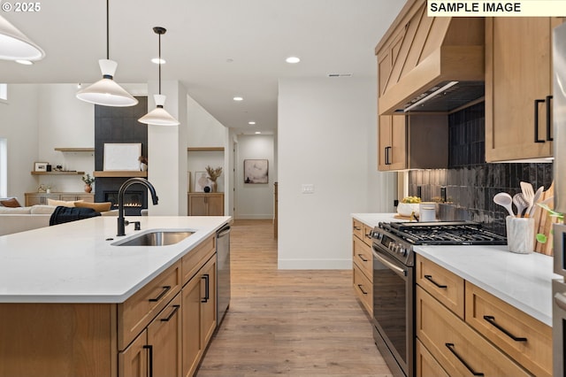 kitchen with pendant lighting, appliances with stainless steel finishes, a sink, an island with sink, and wall chimney exhaust hood