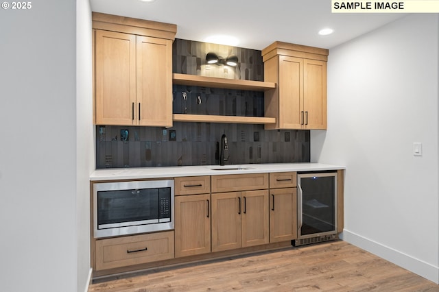 bar with wine cooler, built in microwave, a sink, decorative backsplash, and light wood finished floors