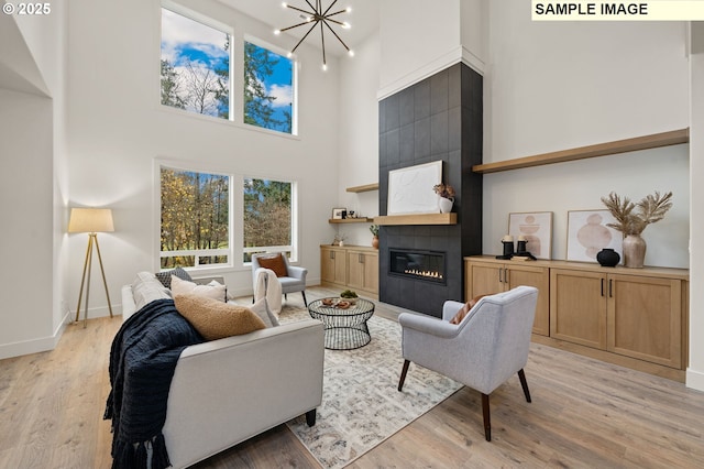 living area with a tile fireplace, a notable chandelier, a high ceiling, baseboards, and light wood finished floors