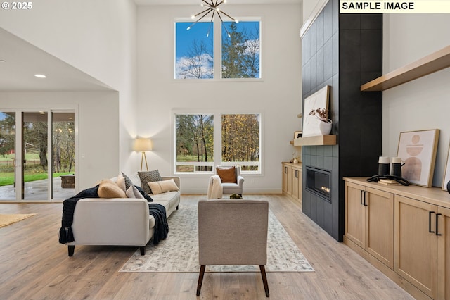 living area featuring baseboards, a fireplace, a towering ceiling, and light wood finished floors