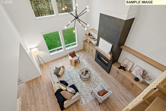 living area featuring light wood-type flooring, a towering ceiling, a notable chandelier, and a glass covered fireplace