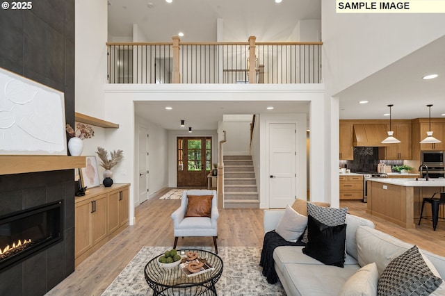 living area featuring baseboards, stairway, a tiled fireplace, and light wood-style floors