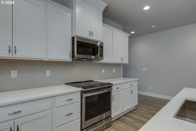 kitchen with sink, stainless steel appliances, tasteful backsplash, white cabinets, and light wood-type flooring