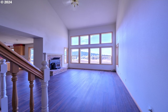 unfurnished living room featuring dark hardwood / wood-style floors, a wood stove, and high vaulted ceiling