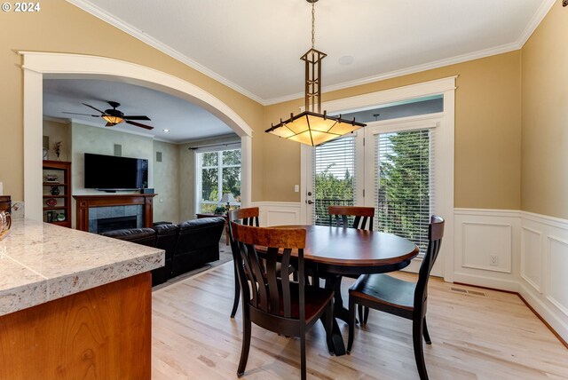 dining room featuring a tile fireplace, ornamental molding, ceiling fan, and light hardwood / wood-style floors