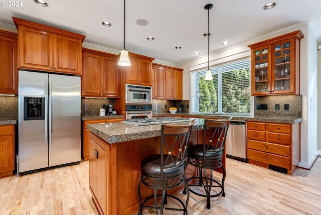 kitchen with a kitchen island, appliances with stainless steel finishes, hanging light fixtures, light hardwood / wood-style floors, and crown molding