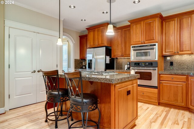 kitchen with ornamental molding, appliances with stainless steel finishes, a center island, and hanging light fixtures