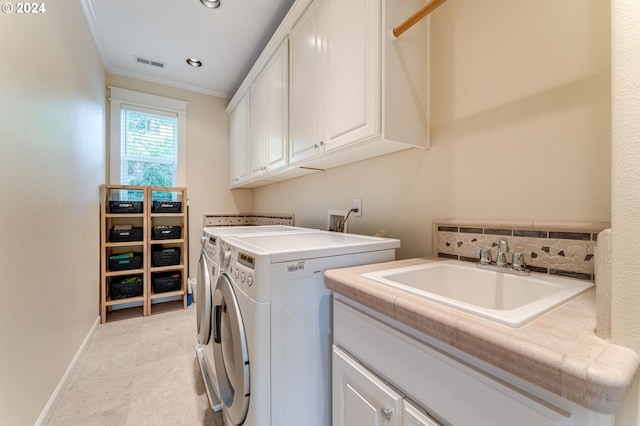 clothes washing area with sink, ornamental molding, cabinets, and washing machine and clothes dryer